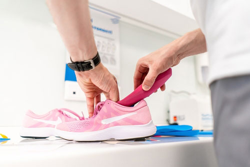 man inserting foot inserts inside a pink shoe